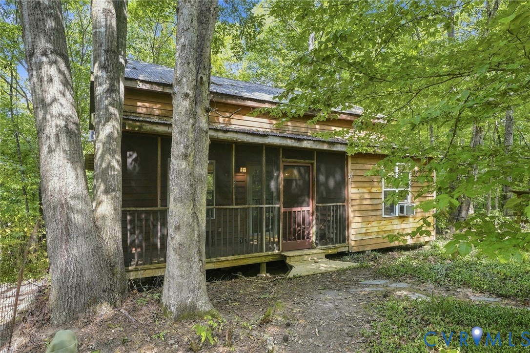Wood-sided home nestled among trees, with a long screened front porch and central entrance.