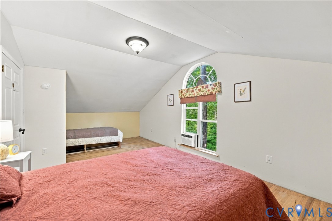 Furnished bedroom with two beds, a sloped ceiling, and an arched window overlooking greenery.