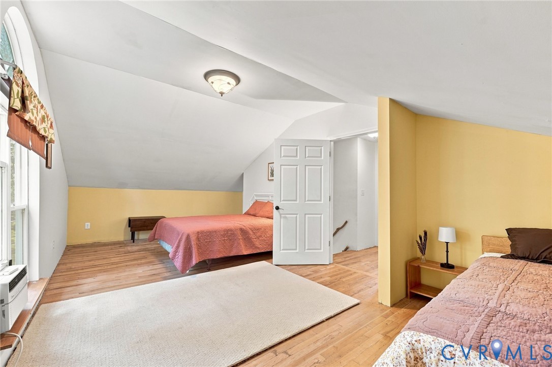 Bedroom with two beds, hardwood floors, yellow walls, and a sloped ceiling.
