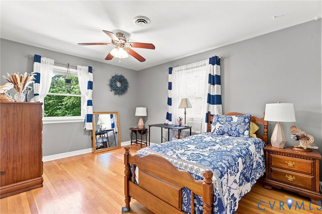 Furnished bedroom with a wooden bed, blue-and-white floral bedding, hardwood floors, and striped curtains.