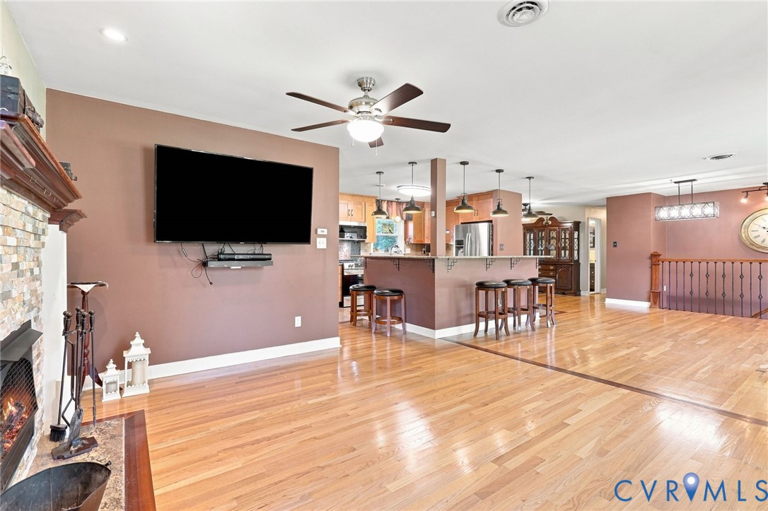 Open-plan living room and kitchen with hardwood floors, stone fireplace, and island seating.
