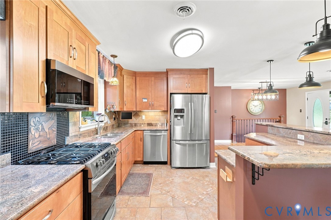 Kitchen with warm wood cabinets, granite counters, stainless appliances, and a large raised breakfast bar.