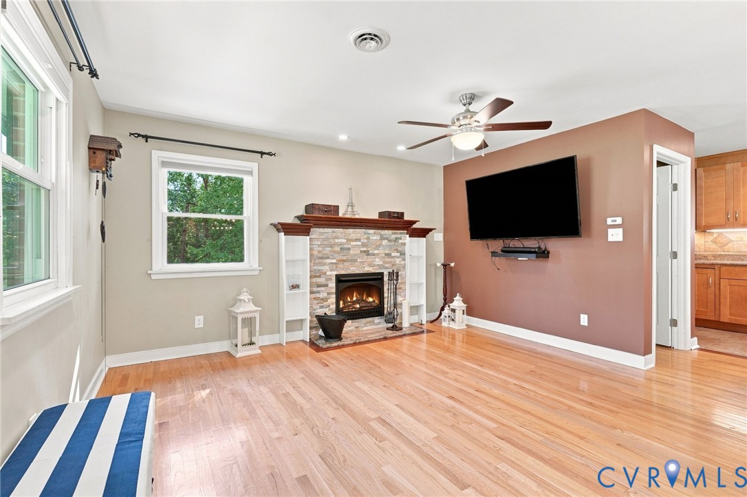 Living room with a stone fireplace, hardwood floors, and a wall-mounted television.
