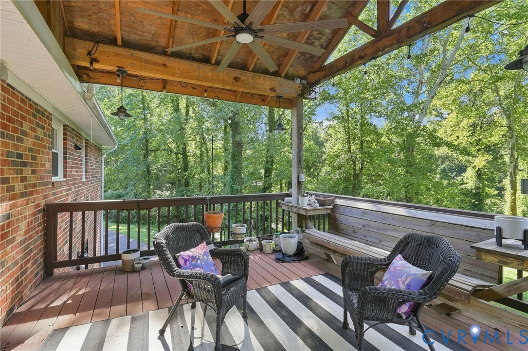 Covered wooden deck with wicker seating and a ceiling fan overlooking trees.