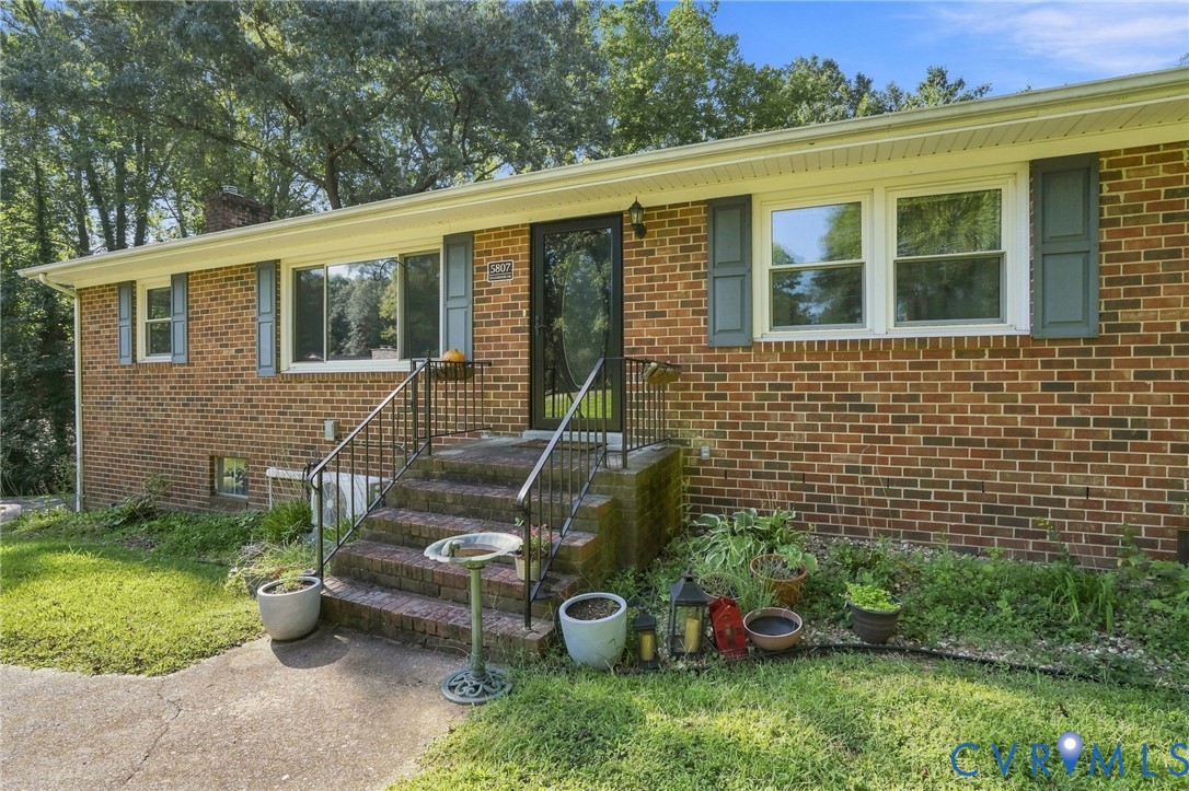 Brick ranch house with a raised front entry, black railings, and mature trees.