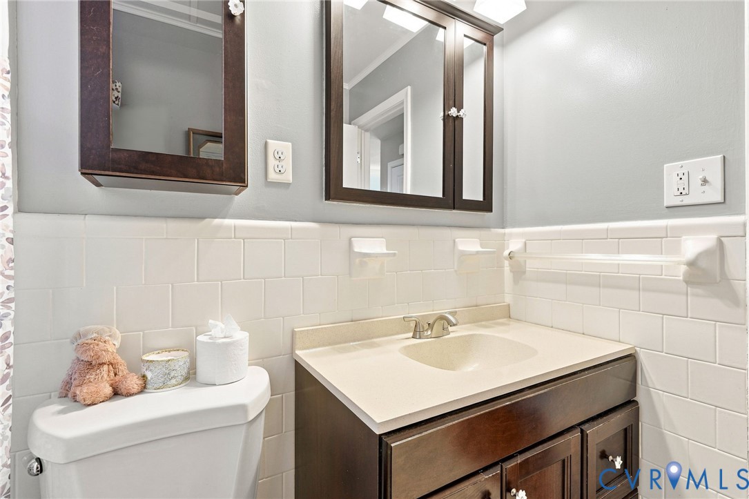 Bathroom with dark wood vanity, cream sink countertop, white tile, and framed mirrors.