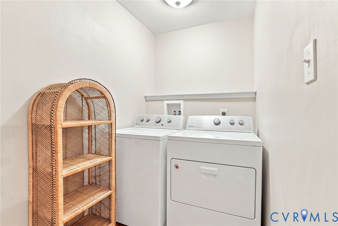 Laundry room with a white washer and dryer beside a tall wicker shelving unit.