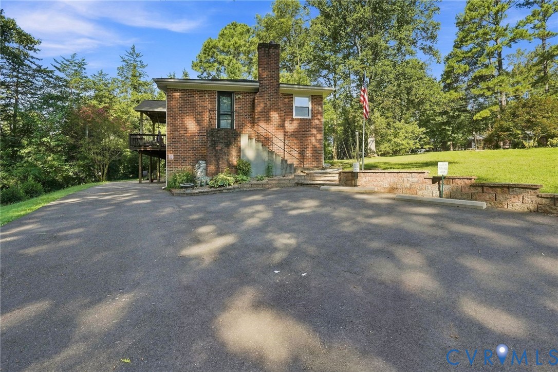 Brick home with exterior stairs, a raised deck, and a broad paved driveway.