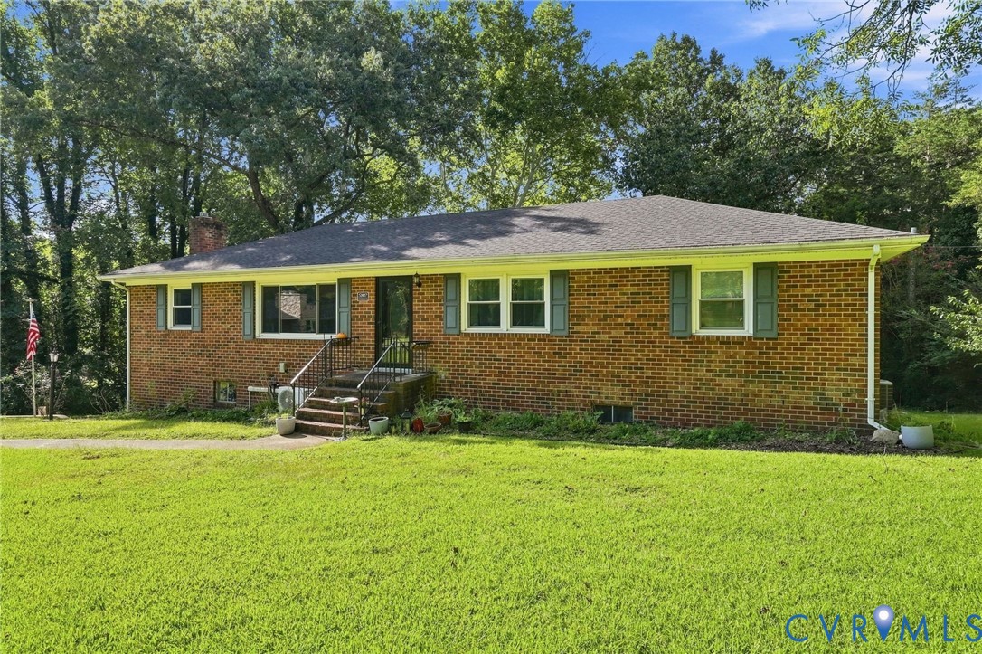 Single-story brick ranch house with pale shutters, front steps, and a broad lawn beneath mature trees.