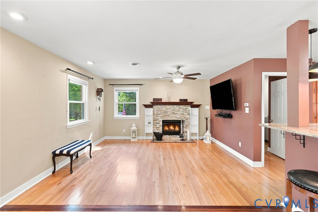 Living room with a stone fireplace, light wood floors, and a striped bench.