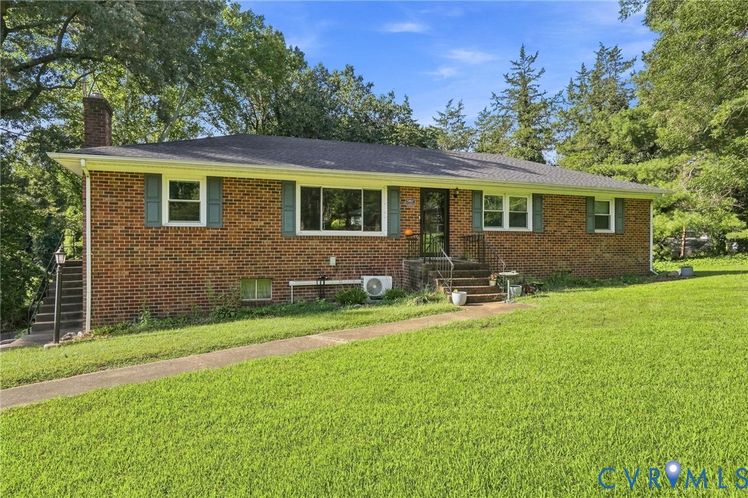 Single-story brick house with gray shutters, a raised central entry, broad lawn, and mature trees.
