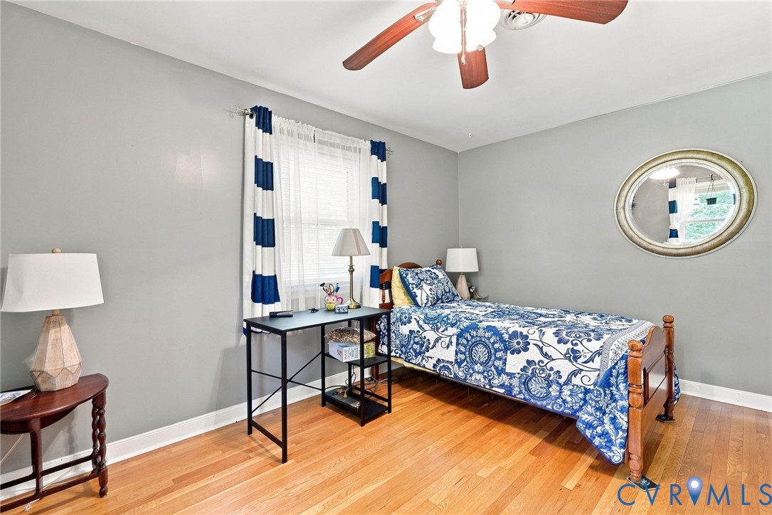 Bedroom with blue-and-white floral bedding, hardwood floors, and an oval wall mirror.