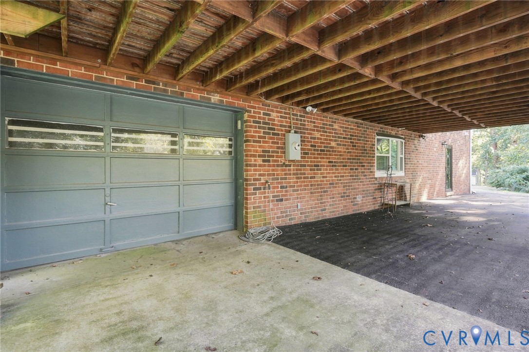 Brick home’s covered parking area with a gray garage door and exposed wooden beams.