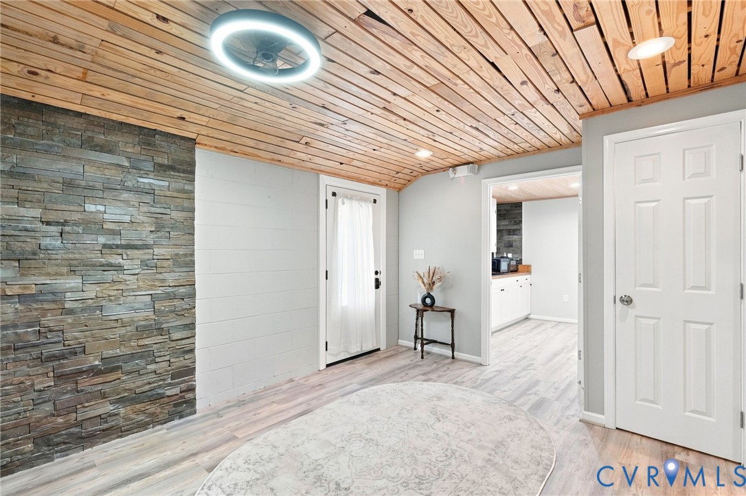 Entry hall with a wood-plank ceiling, stacked-stone wall, and view into the kitchen.