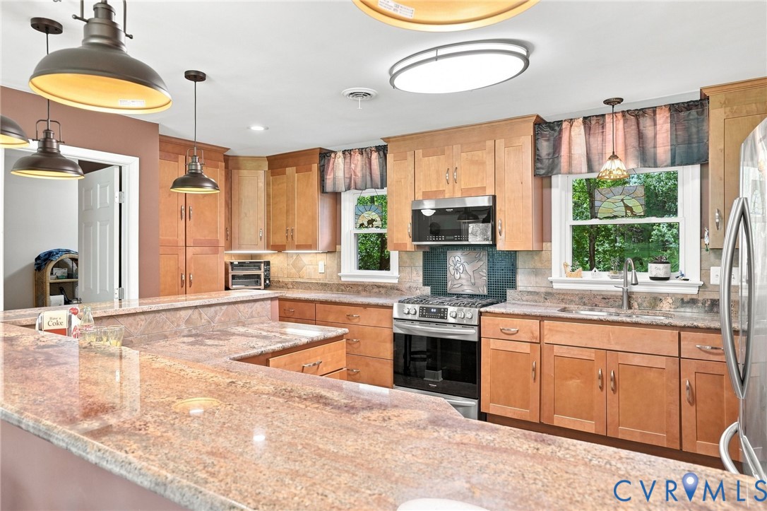 Kitchen with warm wood cabinetry, granite countertops, stainless steel appliances, and windows overlooking greenery.