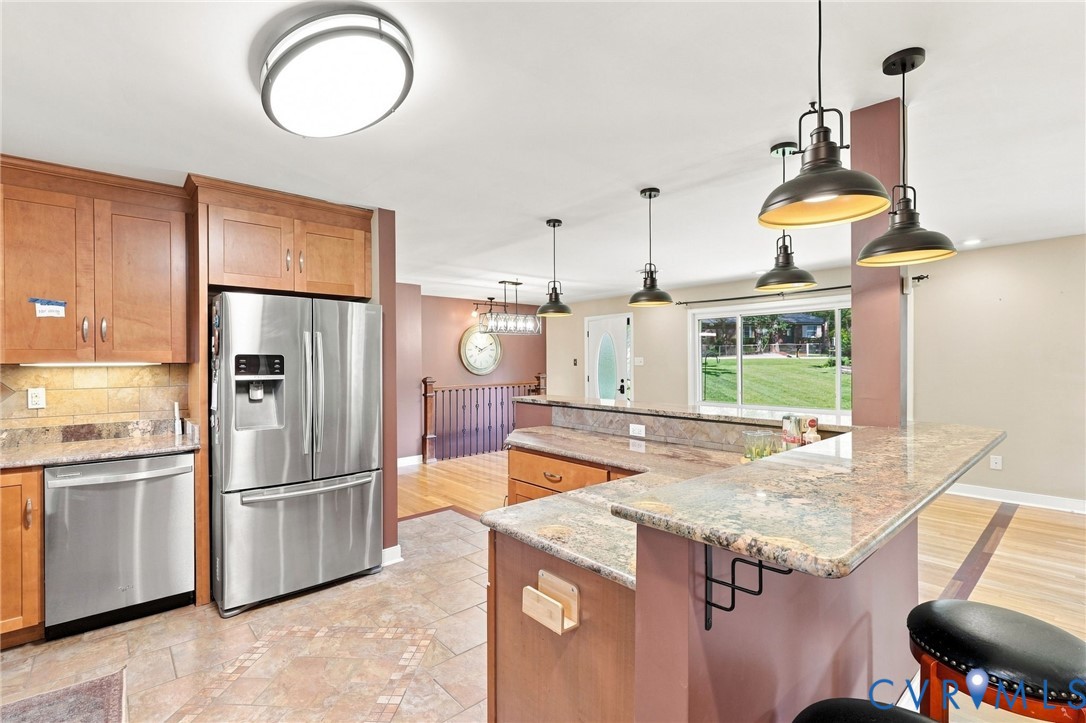 Kitchen with wood cabinets, stainless steel appliances, and a large granite island beneath pendant lights.