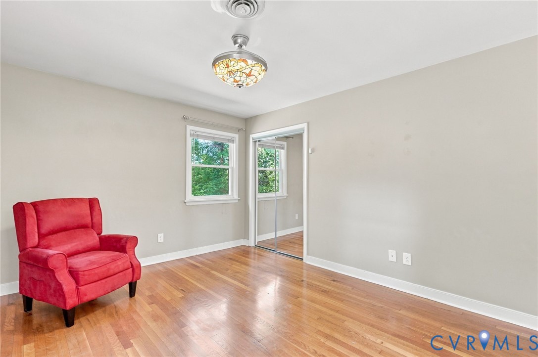 Bedroom with hardwood floors, mirrored closet doors, two windows, and a red armchair.