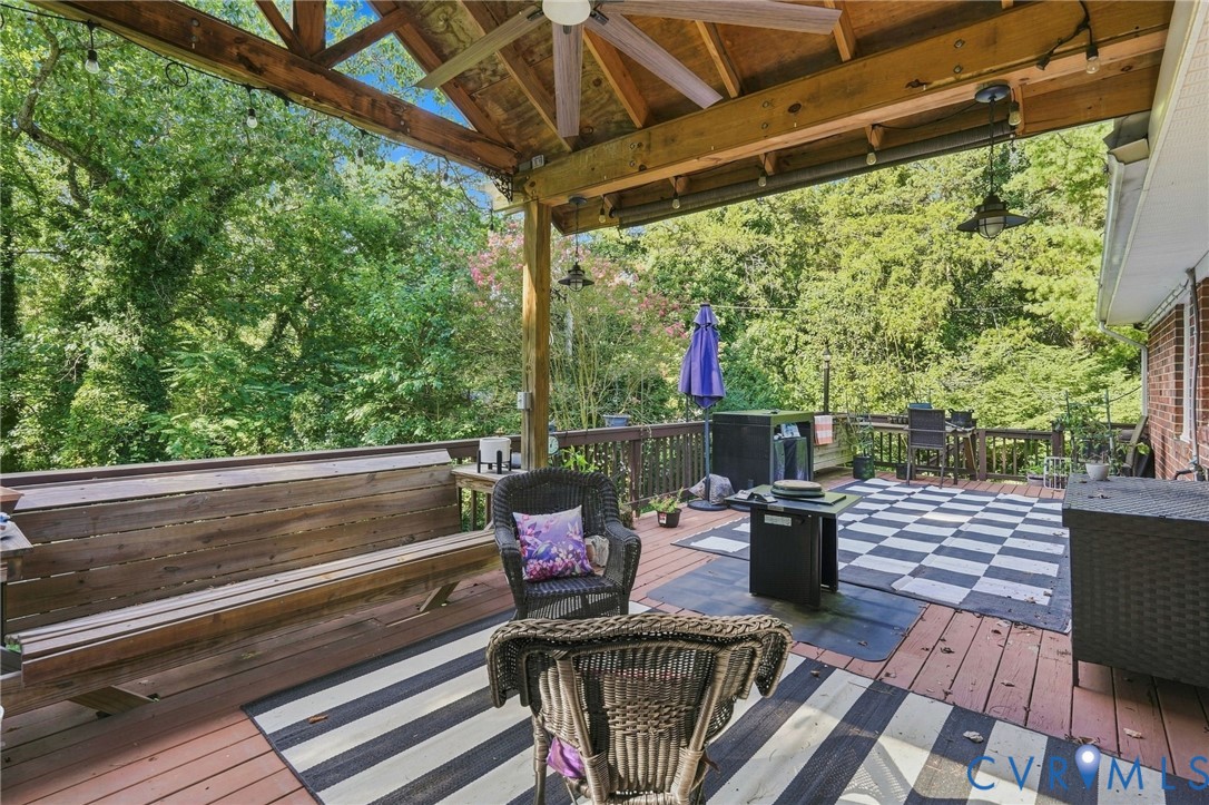 Covered wooden deck with exposed beams, built-in benches, wicker seating, and a checkerboard rug.