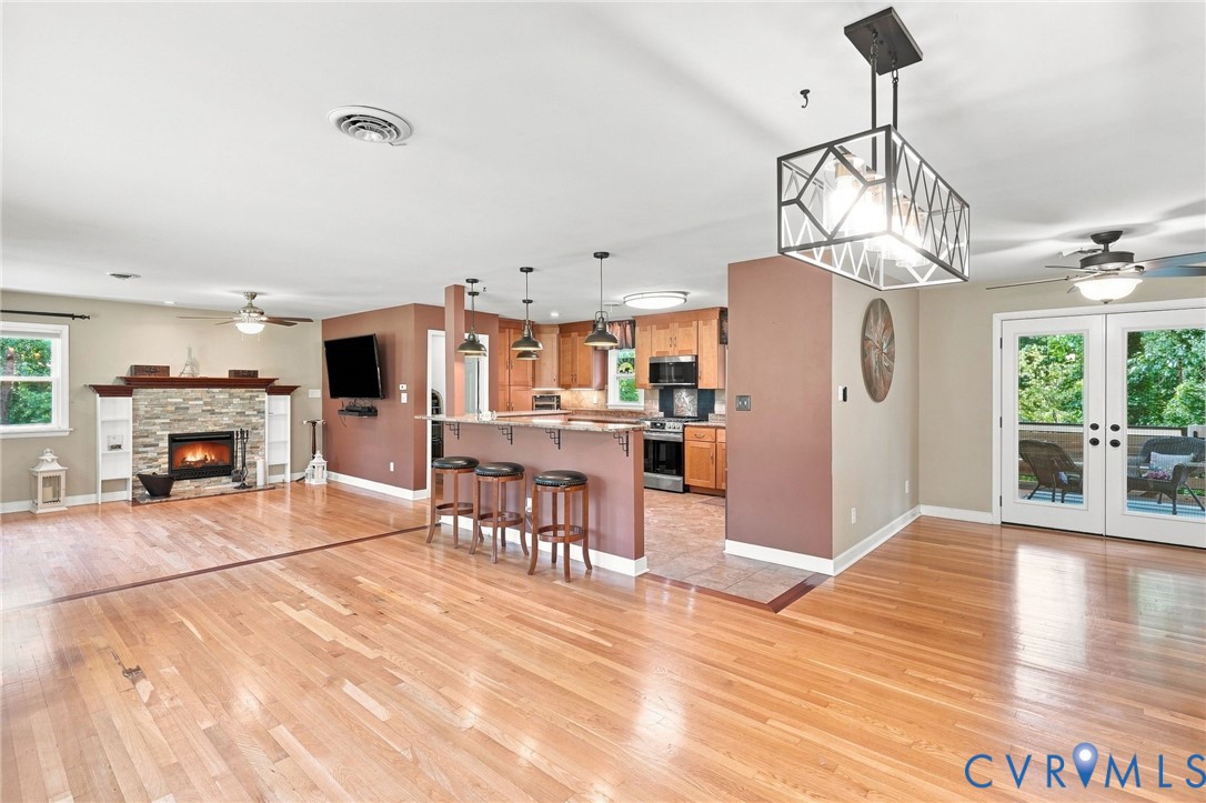 Open-plan living room and kitchen with hardwood floors, stone fireplace, and breakfast bar.