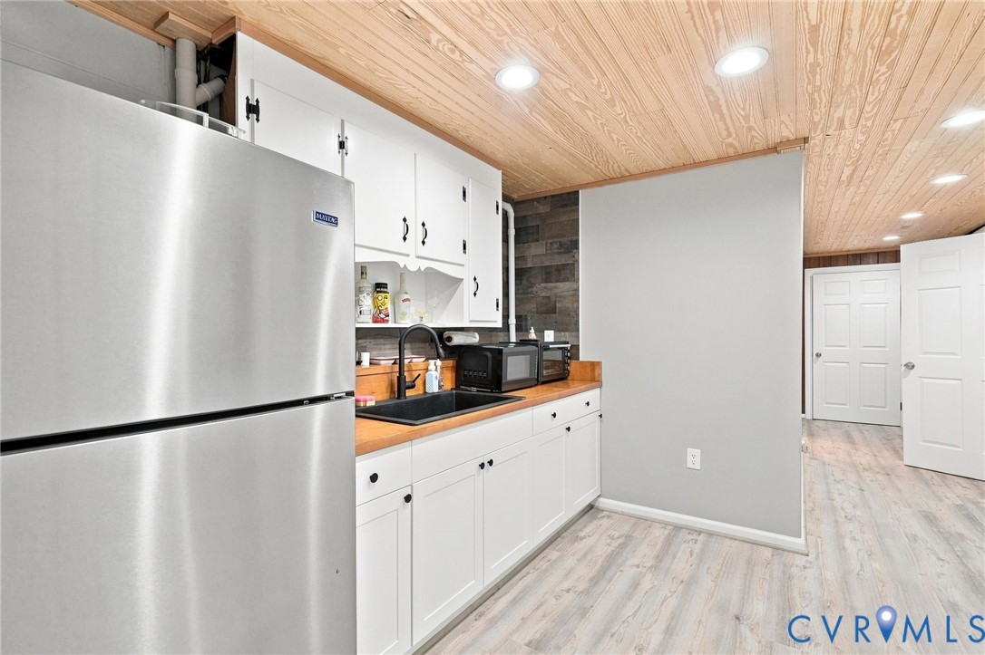 Kitchen with white cabinets, stainless-steel refrigerator, wood countertop, and a wood-plank ceiling.