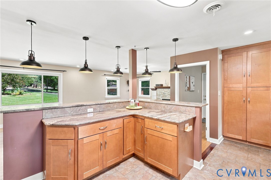 Kitchen with warm wood cabinets, stone counters, a large peninsula, and pendant lights.
