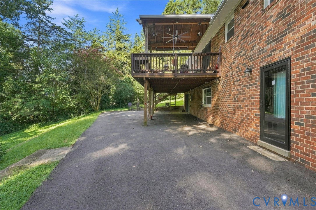 Brick house with a covered elevated deck above a paved patio beside a leafy yard.