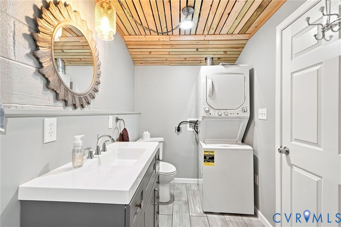 Bathroom with a long white vanity, stacked washer and dryer, and wood-plank ceiling.