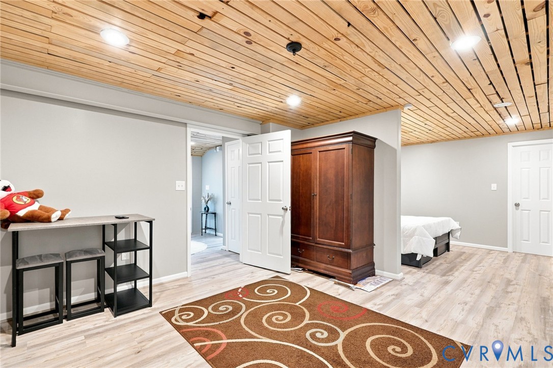 Furnished bedroom with a wood-plank ceiling, dark wardrobe, and bed partly visible at right.