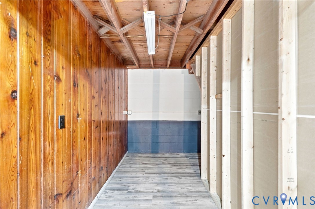 Basement room with gray plank flooring, wood paneling, exposed framing, and a fluorescent light.