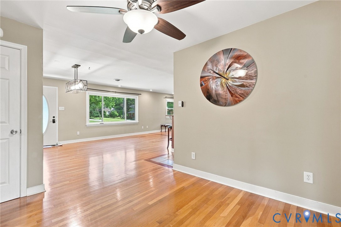 Open living area with polished hardwood floors, ceiling fan, and large window overlooking greenery.