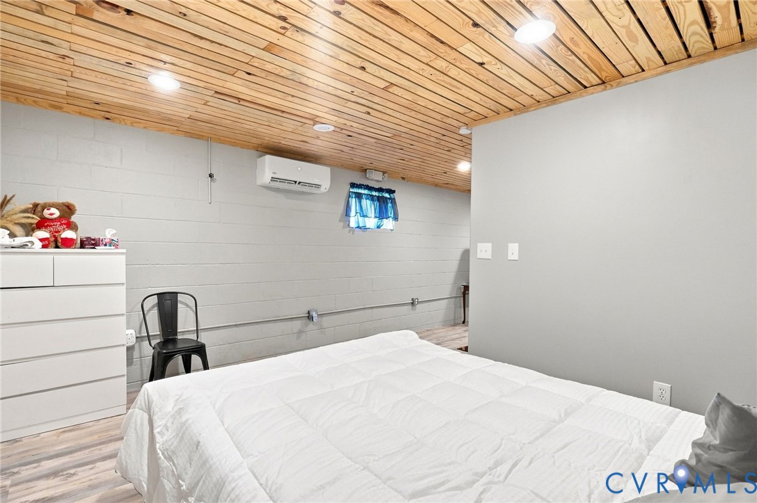 Bedroom with a white bed beneath a distinctive light wood plank ceiling and blue-curtained window.
