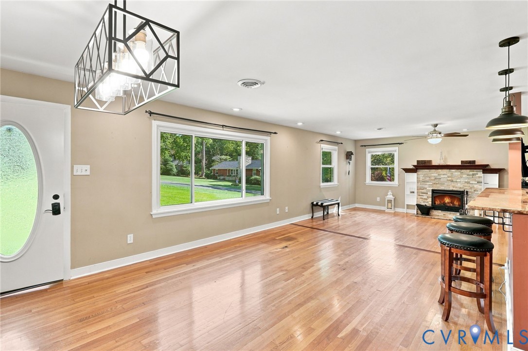 Open living and dining area with hardwood floors, large windows, and a stone-surround fireplace.