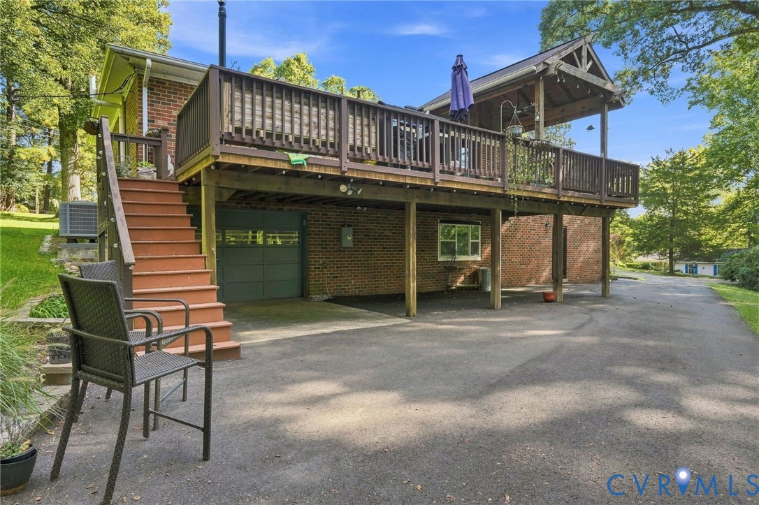 Rear exterior of a brick home with a raised wooden deck, stairs, and driveway.