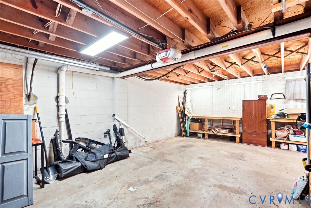 Garage workshop with exposed wooden rafters, concrete floor, workbenches, and storage cabinets.