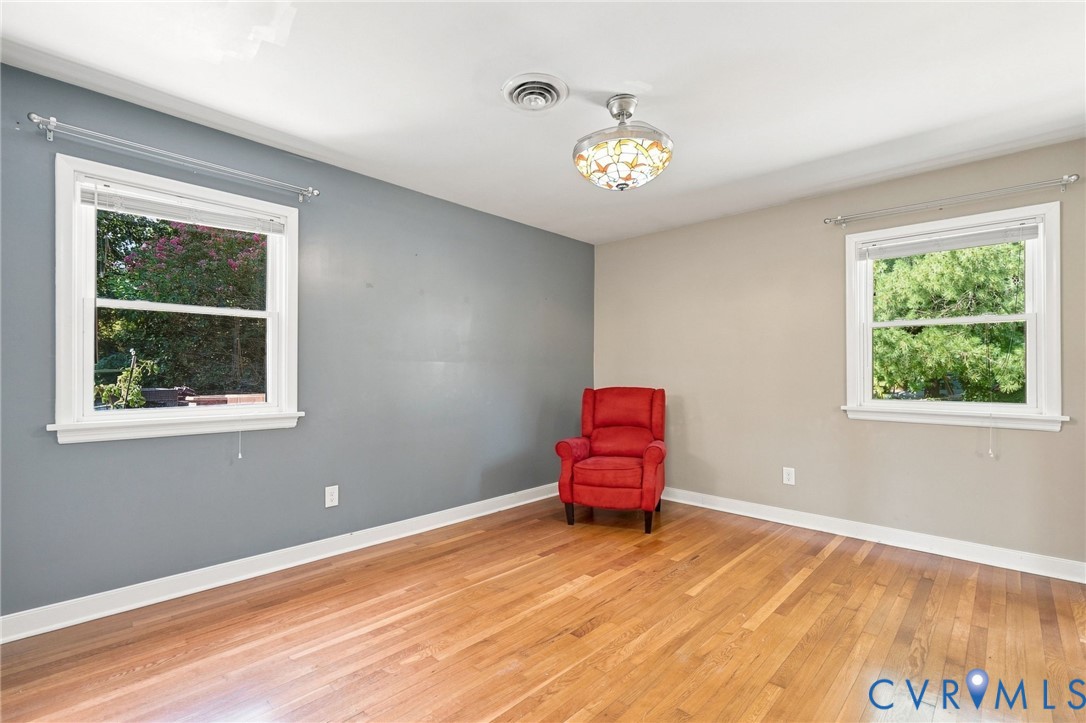 Room with hardwood floors, two windows, and a red armchair.