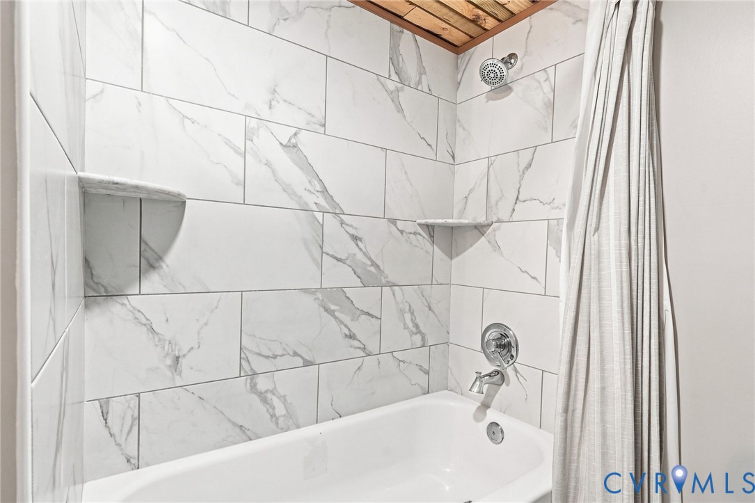 Bathroom with a white tub, marble-look tile, and a wood-plank ceiling.