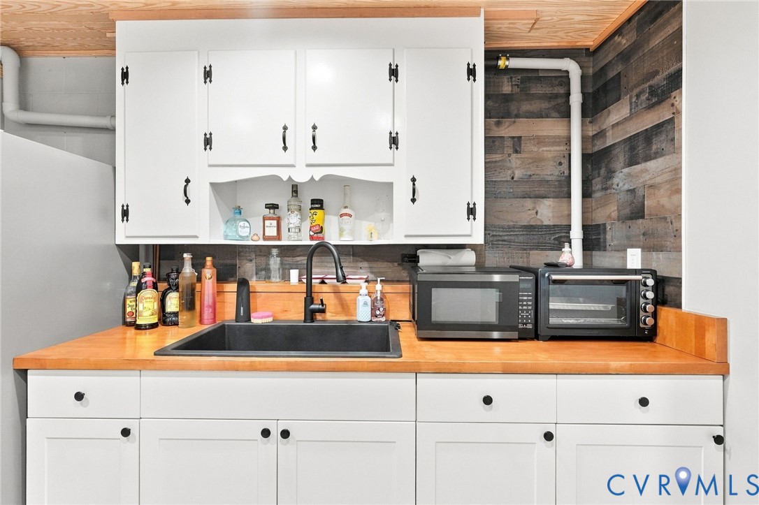 Kitchen with white cabinets, a black sink, wood countertop, and rustic plank backsplash.
