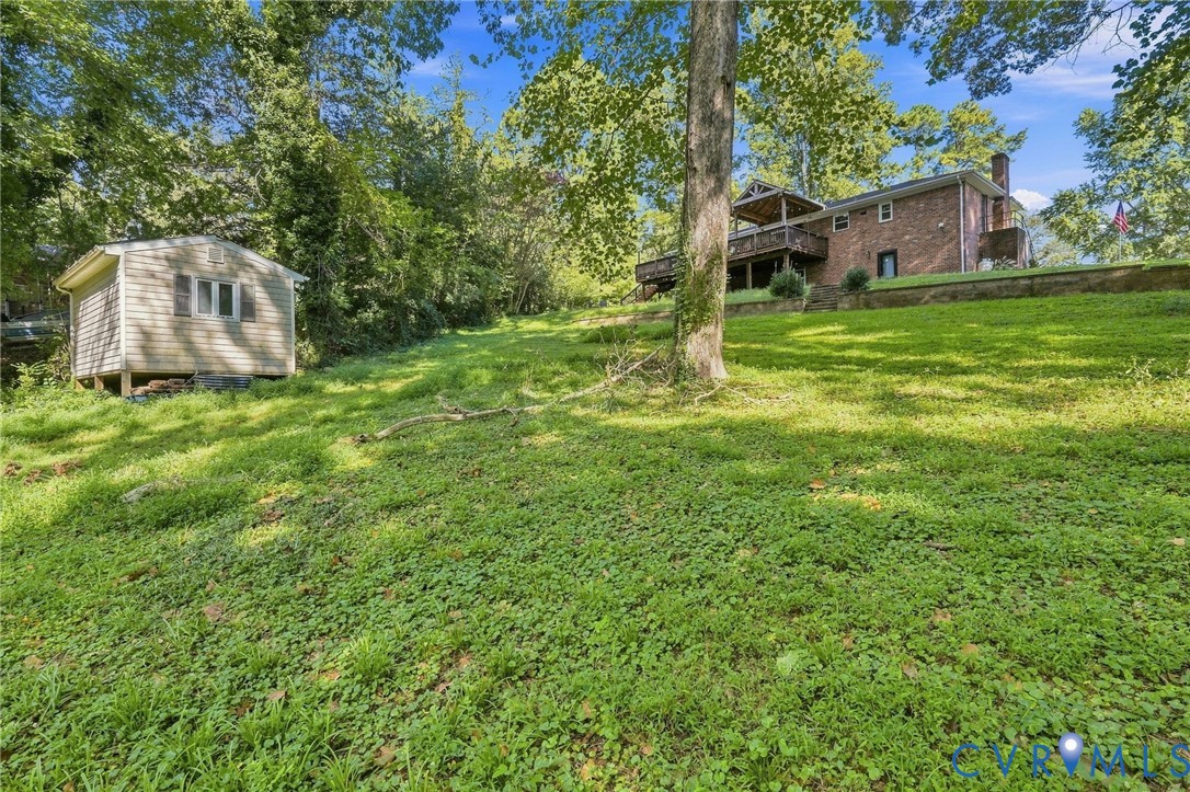 Brick home with a raised deck above a sloping lawn, surrounded by mature trees and a detached shed.