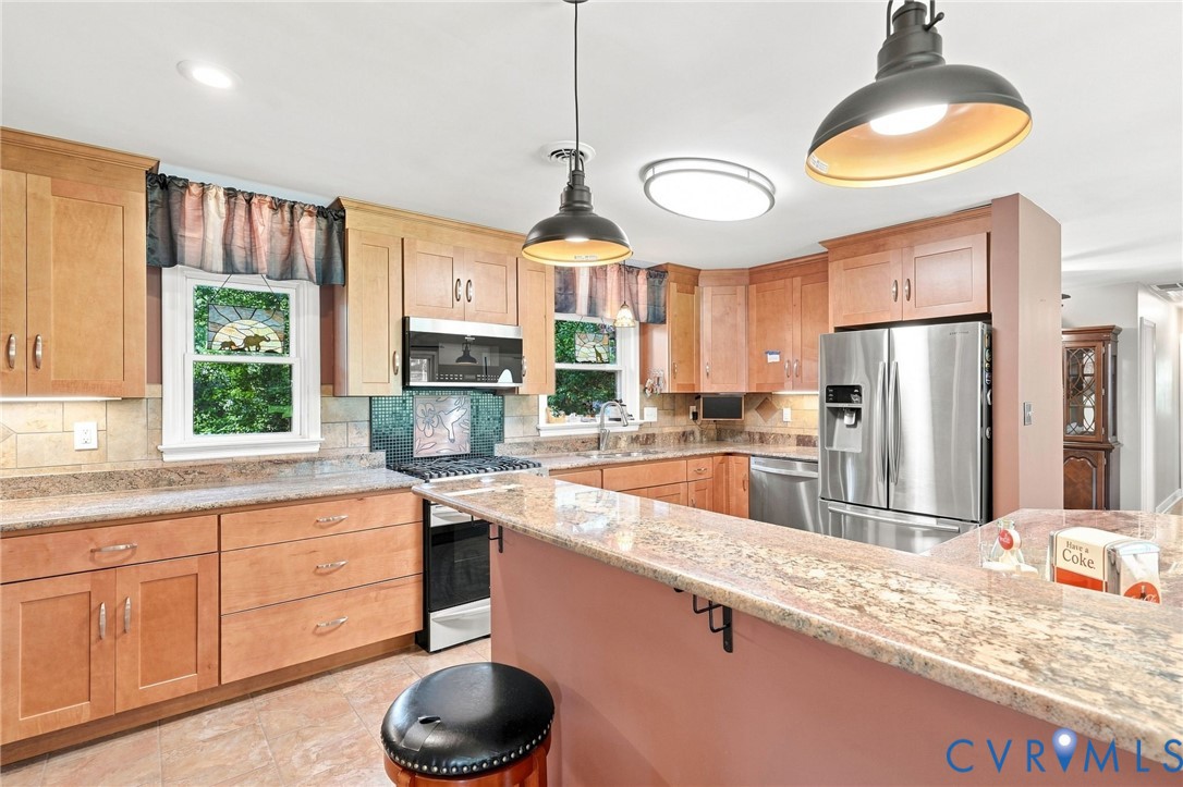 Kitchen with honey-toned cabinets, granite peninsula, stainless steel appliances, and pendant lights.