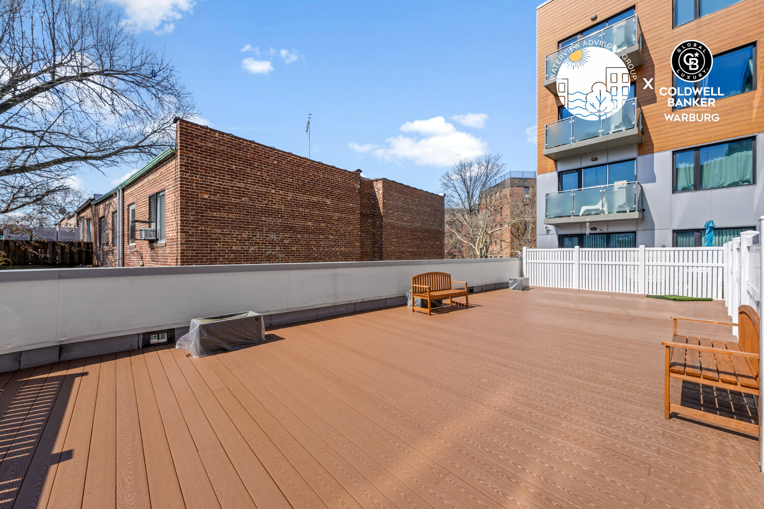 Rooftop deck with wooden benches, brown plank flooring, and a white privacy fence.