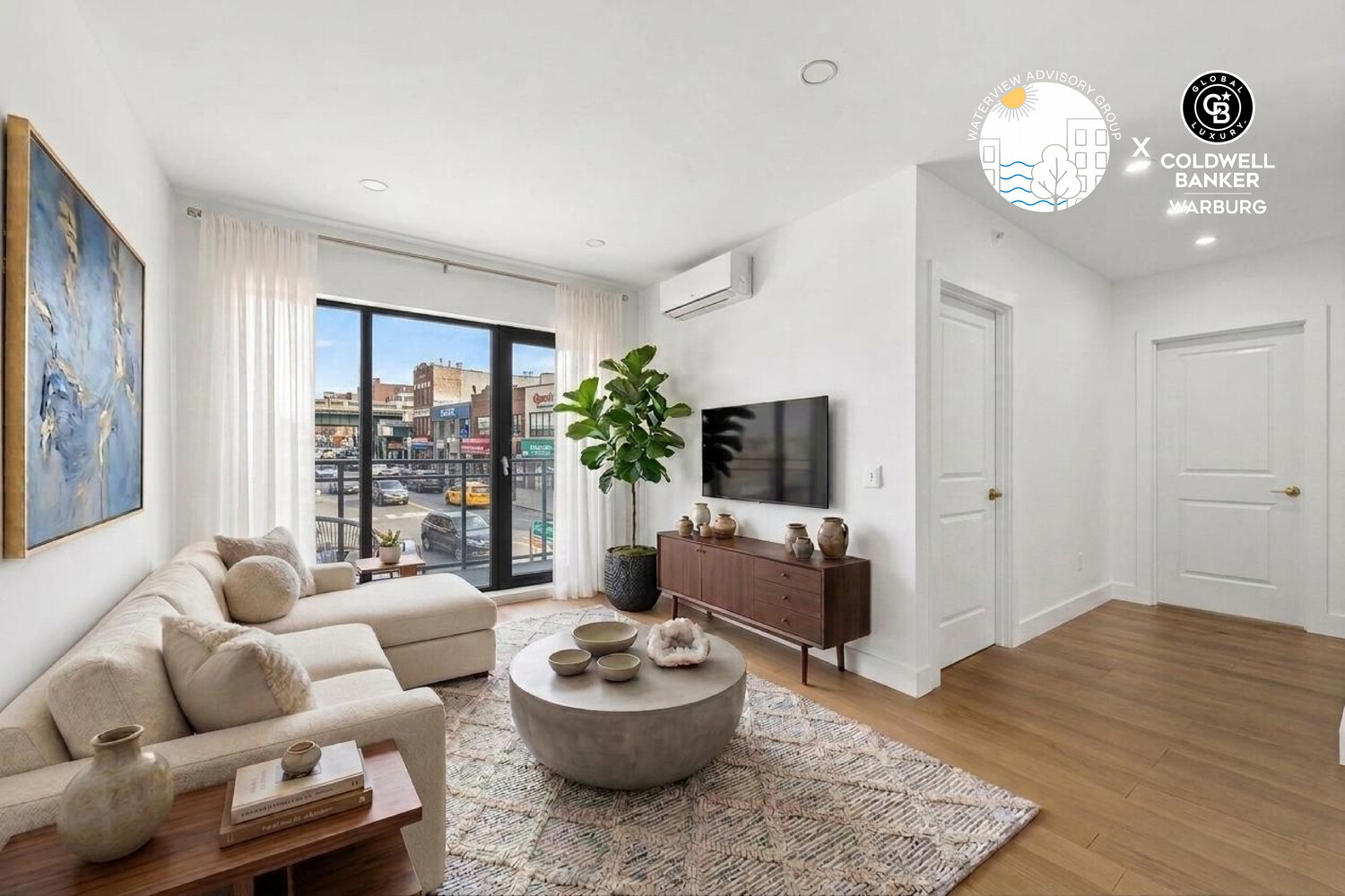 Staged living room with a cream sectional, round coffee table, and glass doors overlooking the street.