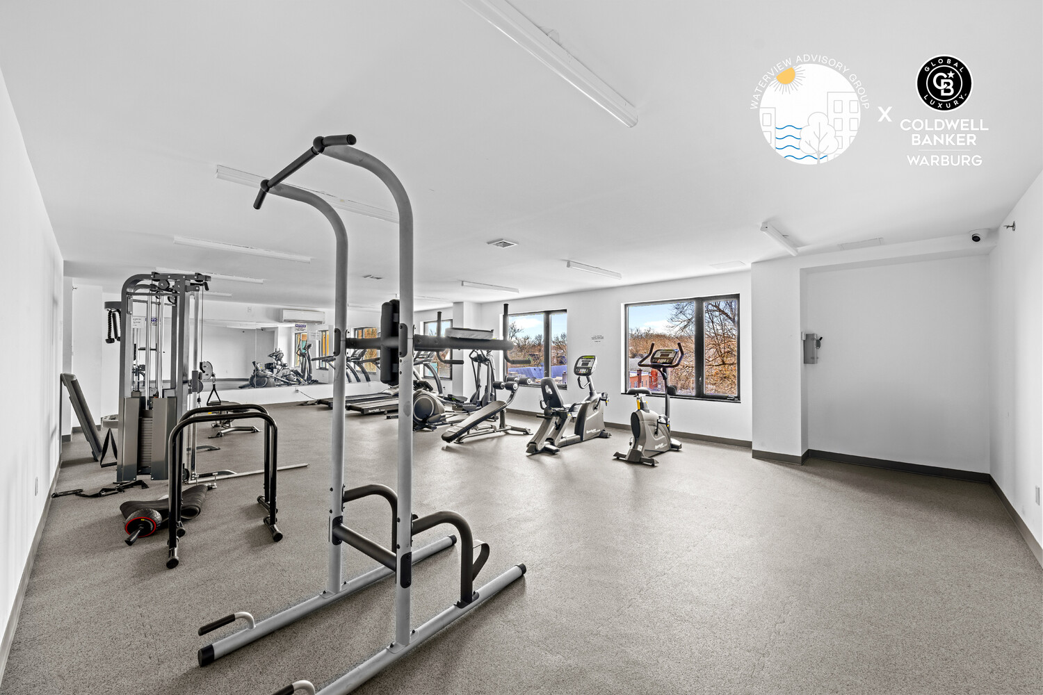 Fitness room with exercise machines and stationary bikes beside large windows.