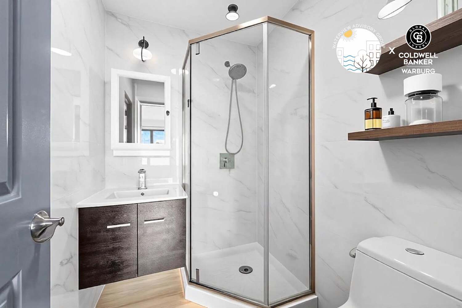 Renovated bathroom with a glass shower, marble-look walls, and dark wood vanity.