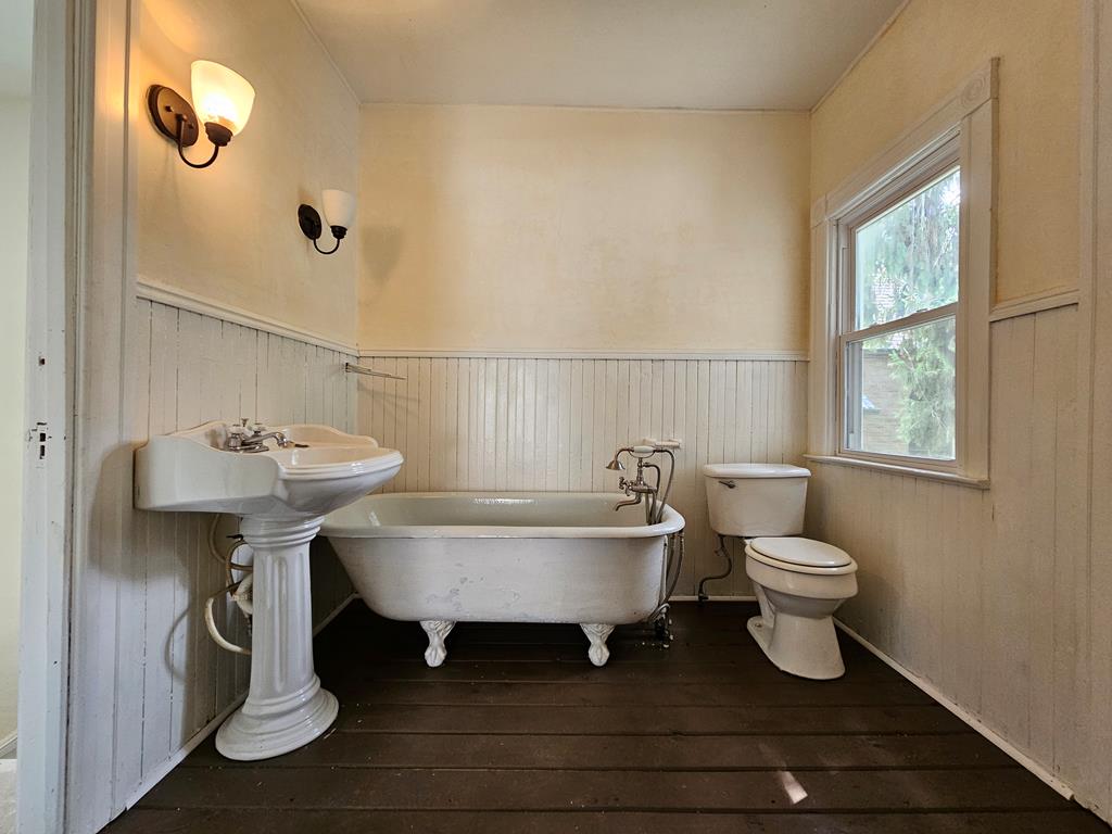 Bathroom with a clawfoot tub, pedestal sink, and cream beadboard wainscoting.