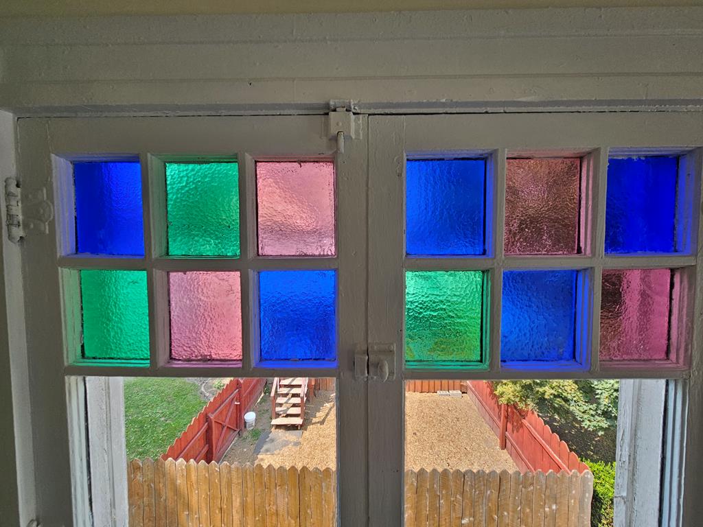 Divided-light window with colorful textured glass panes above a view of the fenced yard.