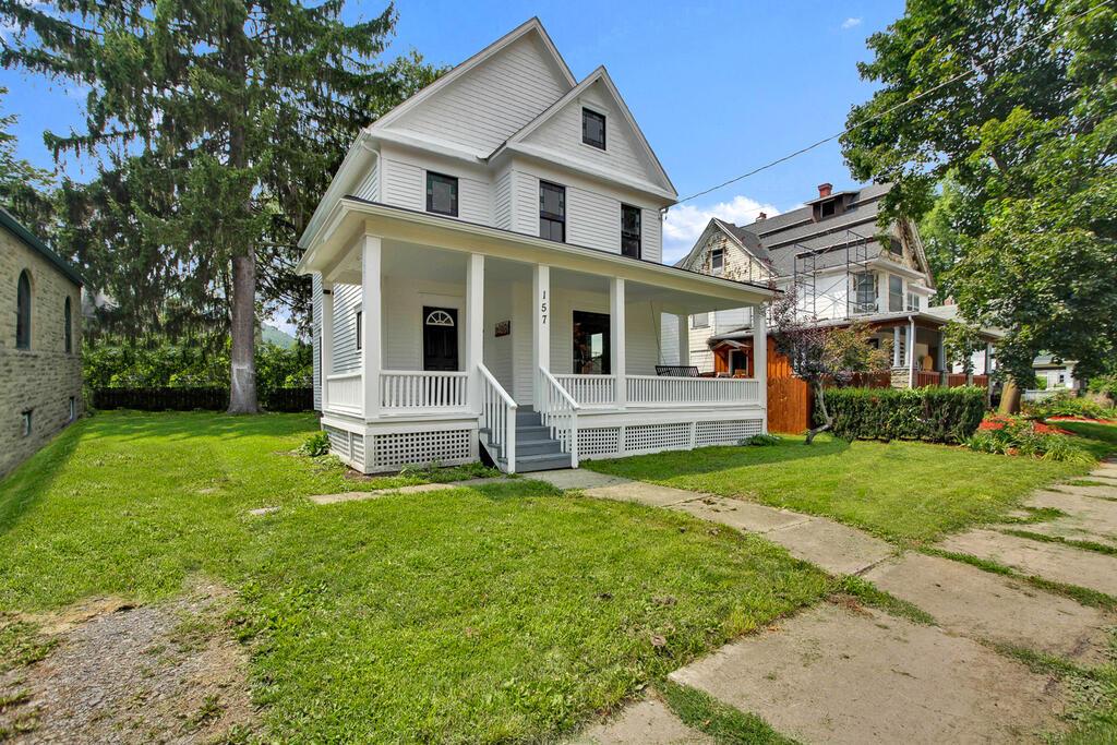 White two-story house with a broad covered porch, front steps, and a grassy lawn.