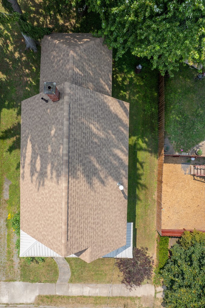 Aerial view of a house with a broad tan shingle roof and chimney, surrounded by trees and lawn.