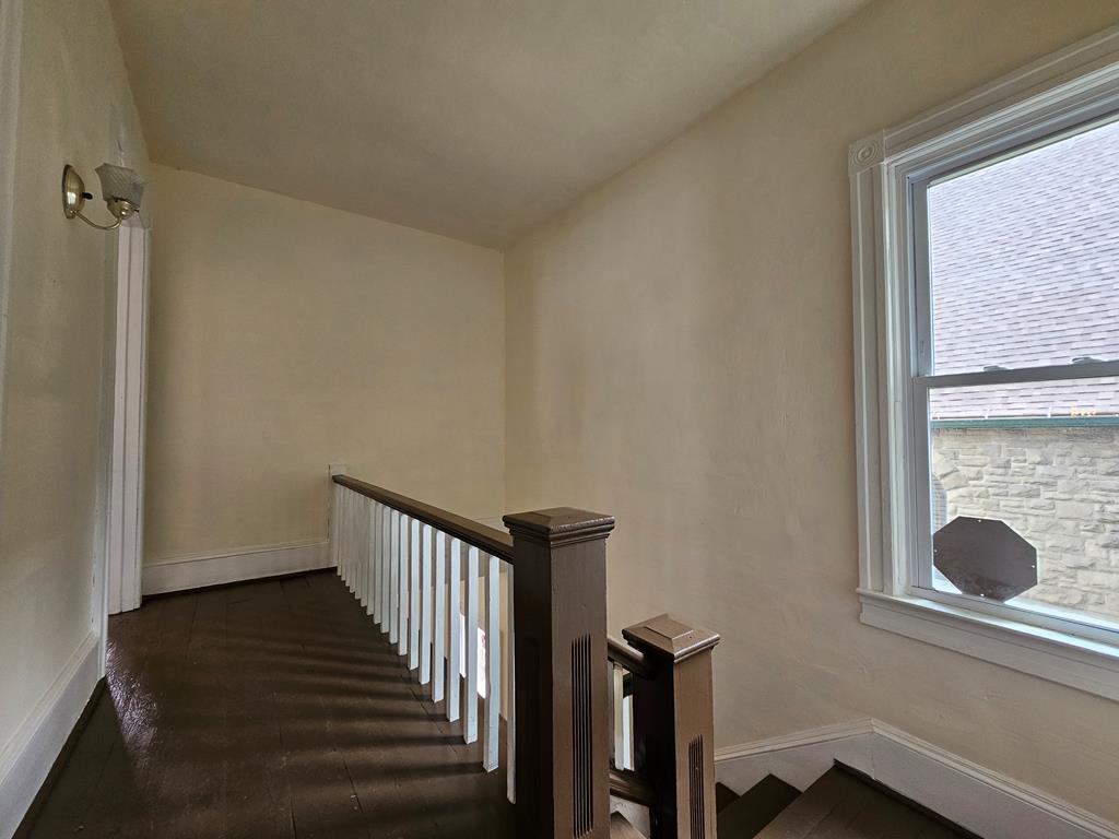 Upstairs hallway with dark wood floors, a contrasting stair railing, and a large window.