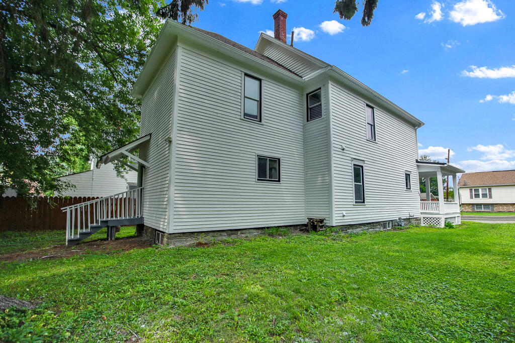 White two-story house with porches on both sides, a brick chimney, and a green lawn.