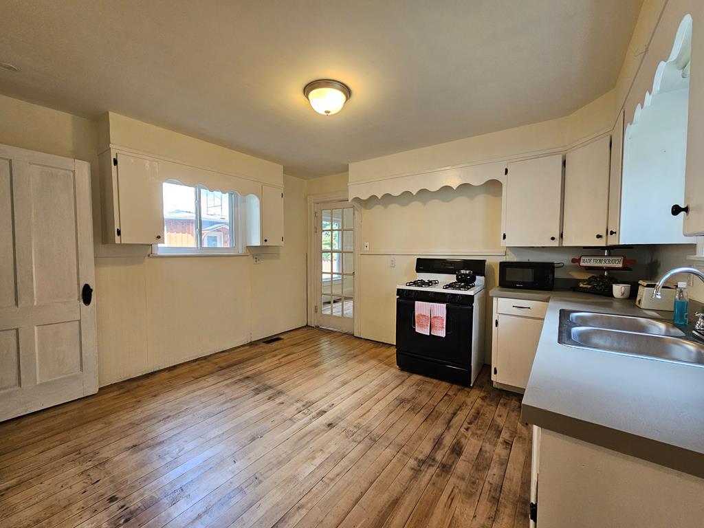 Kitchen with white cabinetry, a black gas range, and worn wide-plank wood floors.